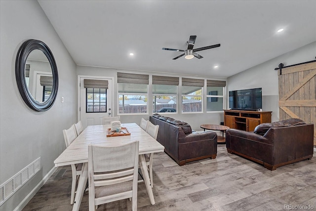 dining room with a barn door, visible vents, light wood-style flooring, and a ceiling fan