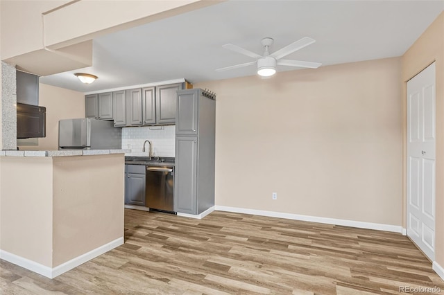 kitchen featuring gray cabinets, appliances with stainless steel finishes, wood-type flooring, sink, and decorative backsplash