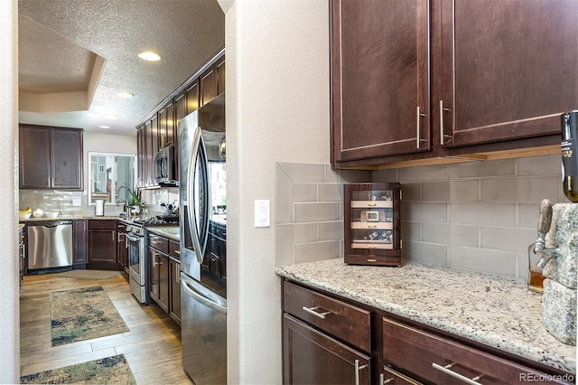 kitchen with a textured ceiling, light wood-type flooring, backsplash, light stone countertops, and appliances with stainless steel finishes