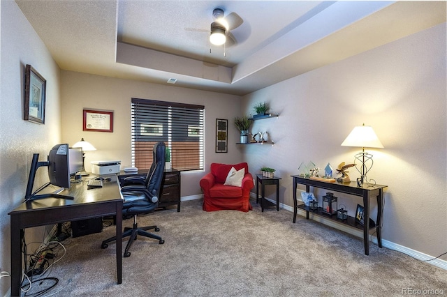 carpeted office space with a tray ceiling, ceiling fan, and baseboards