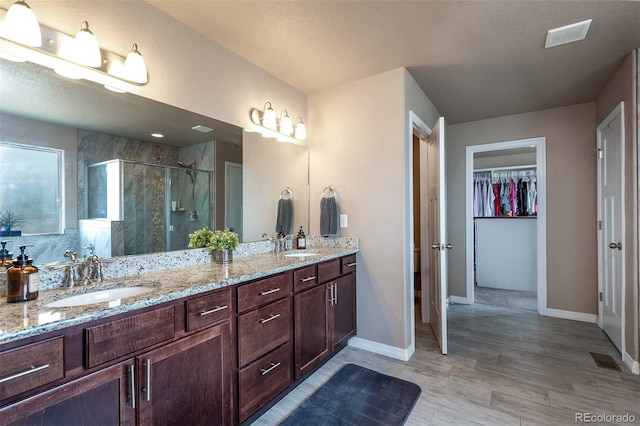 full bath featuring a sink, double vanity, a spacious closet, and a stall shower