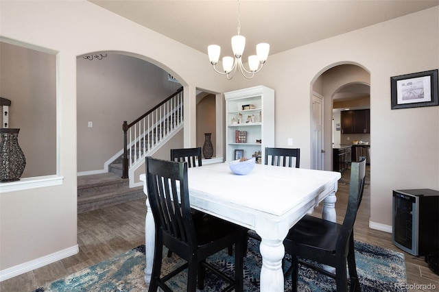 dining room featuring wine cooler, a chandelier, arched walkways, dark wood-style floors, and baseboards