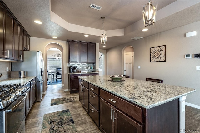 kitchen with stainless steel range with gas cooktop, a raised ceiling, arched walkways, decorative backsplash, and a kitchen island