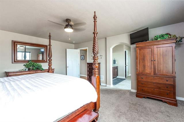 bedroom with arched walkways, light carpet, ensuite bath, and baseboards