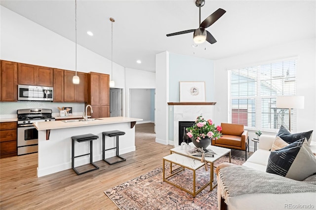 living room featuring a tiled fireplace, ceiling fan, high vaulted ceiling, light hardwood / wood-style floors, and sink