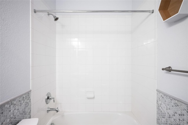 bathroom featuring toilet, tile walls, and tiled shower / bath