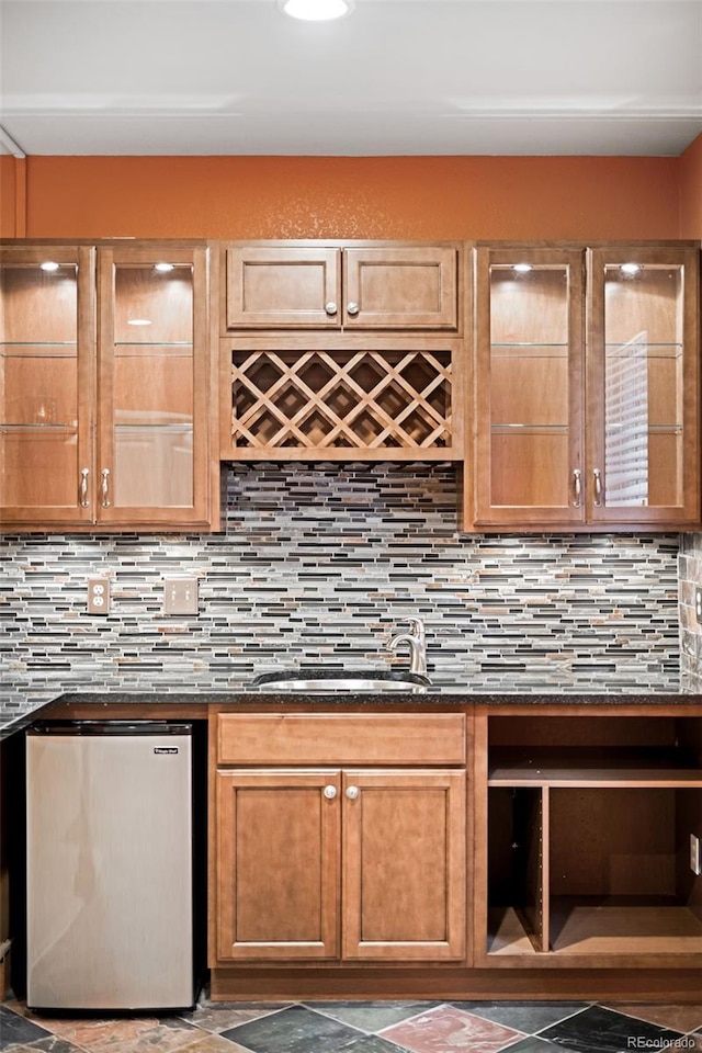 kitchen with dark stone countertops, sink, backsplash, and stainless steel fridge