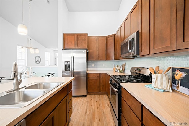 kitchen with light wood-type flooring, a sink, decorative light fixtures, stainless steel appliances, and light countertops