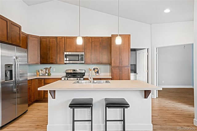 kitchen with a sink, stainless steel appliances, light countertops, a kitchen breakfast bar, and light wood-type flooring