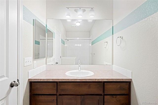 full bath featuring visible vents, tiled shower, and vanity