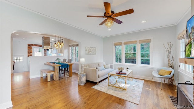 living room with light hardwood / wood-style floors, crown molding, plenty of natural light, and ceiling fan with notable chandelier