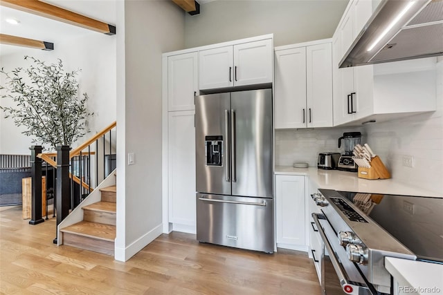 249 E Coyote Ct, Silverthorne, CO 80498 - kitchen featuring appliances with stainless steel finishes, wall chimney exhaust hood, light wood finished floors, tasteful backsplash, and beamed ceiling
