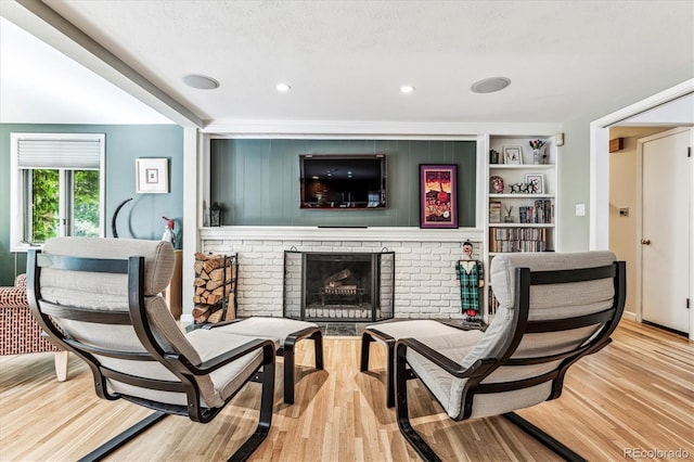 living area featuring built in features, a brick fireplace, light hardwood / wood-style floors, and a textured ceiling