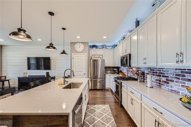 kitchen featuring dark hardwood / wood-style floors, appliances with stainless steel finishes, white cabinets, a center island with sink, and sink