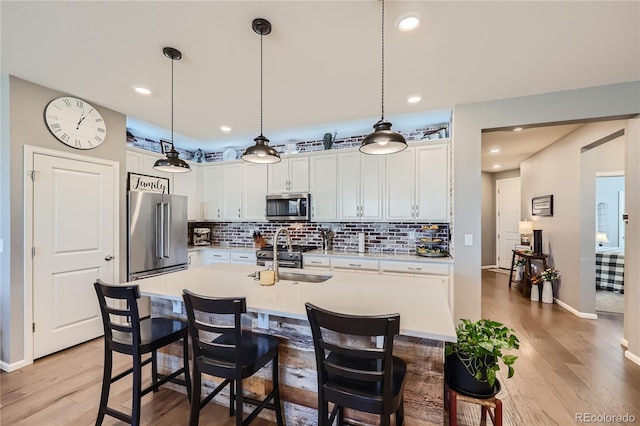 kitchen featuring high quality appliances, an island with sink, wood-type flooring, and white cabinets