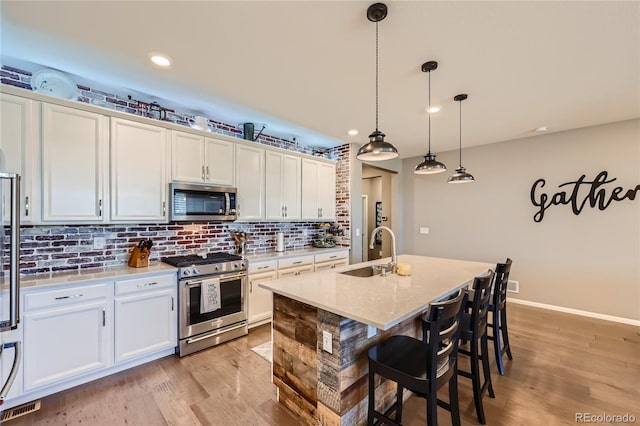 kitchen featuring appliances with stainless steel finishes, light wood-type flooring, decorative backsplash, and pendant lighting