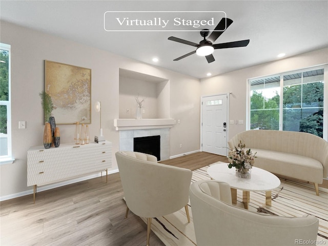 living room featuring light wood-type flooring, ceiling fan, and a fireplace