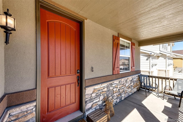 entrance to property featuring covered porch, stone siding, and stucco siding