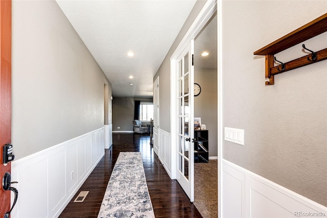 corridor featuring a wainscoted wall, french doors, and dark wood-style floors