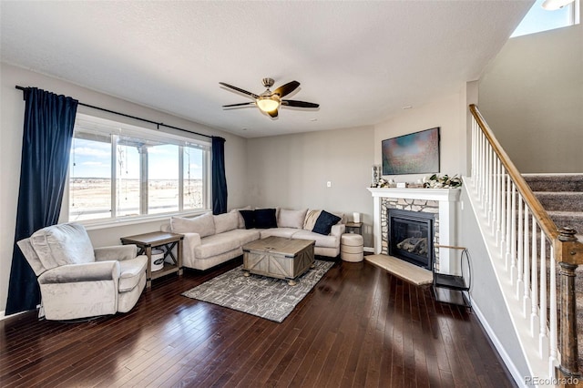 living area featuring baseboards, a ceiling fan, hardwood / wood-style flooring, stairs, and a fireplace