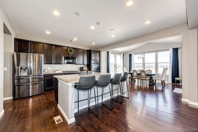 kitchen featuring black microwave, a kitchen island with sink, a sink, dark brown cabinets, and stainless steel fridge with ice dispenser