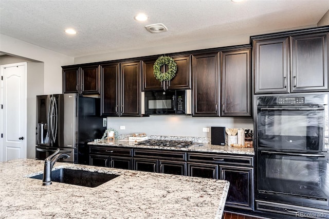 kitchen with light stone countertops, black appliances, visible vents, and a sink