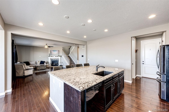 kitchen with light stone counters, freestanding refrigerator, a glass covered fireplace, a sink, and dishwasher