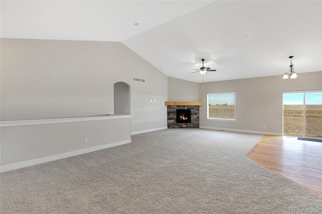 unfurnished living room featuring ceiling fan, a stone fireplace, lofted ceiling, and light carpet