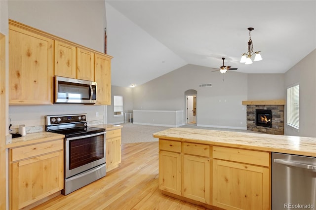 kitchen with light brown cabinets, light hardwood / wood-style flooring, a fireplace, ceiling fan with notable chandelier, and appliances with stainless steel finishes