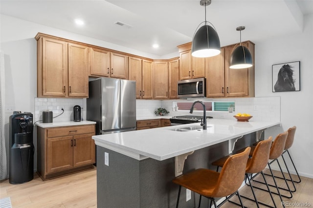 kitchen with stainless steel appliances, light wood-type flooring, backsplash, decorative light fixtures, and kitchen peninsula