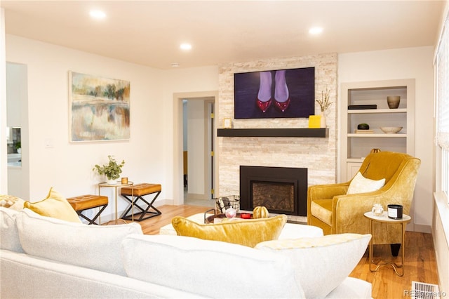 living room featuring built in shelves, a stone fireplace, and light hardwood / wood-style flooring