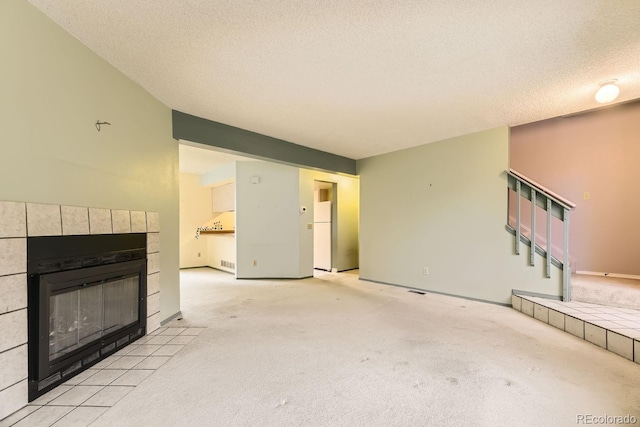 unfurnished living room with a tiled fireplace, light carpet, and a textured ceiling