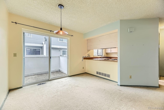 unfurnished living room with light carpet, a textured ceiling, and sink