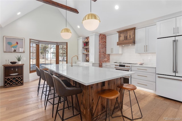 kitchen featuring high end appliances, open shelves, a sink, light wood-type flooring, and backsplash