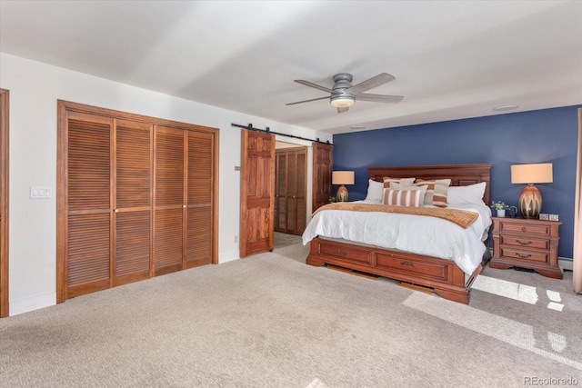 bedroom with two closets, a baseboard heating unit, ceiling fan, a barn door, and carpet floors