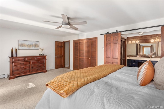 bedroom with ensuite bathroom, a barn door, carpet floors, a closet, and ceiling fan