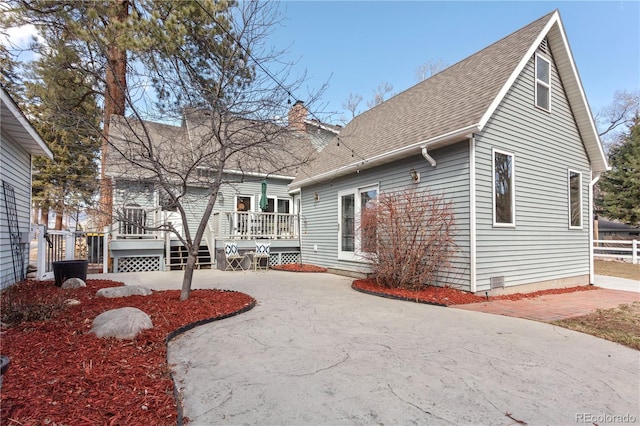 rear view of property with a wooden deck, a shingled roof, a chimney, and a patio area