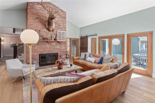 living room featuring a barn door, high vaulted ceiling, a fireplace, and hardwood / wood-style flooring