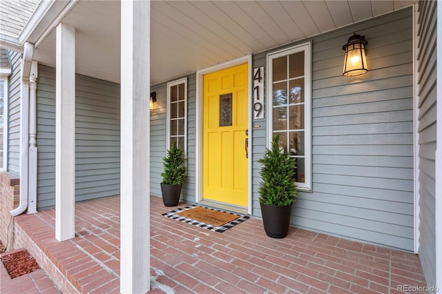 doorway to property with brick siding, covered porch, and a shingled roof