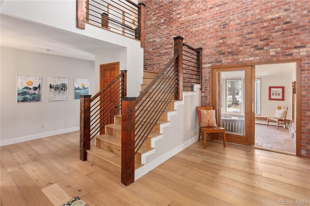 staircase with baseboards, wood-type flooring, a towering ceiling, and brick wall