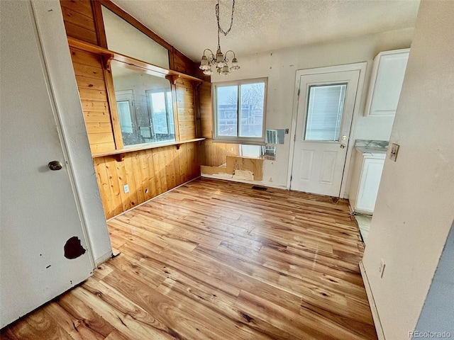 interior space with a notable chandelier, wood walls, a textured ceiling, vaulted ceiling, and light wood-type flooring