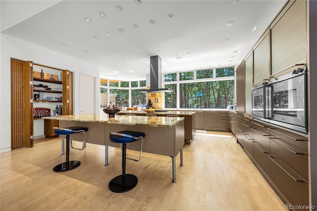 1250 Dolan Dr, Monument, CO 80132 - kitchen featuring island exhaust hood, a large island, light wood-style floors, a kitchen breakfast bar, and light stone countertops