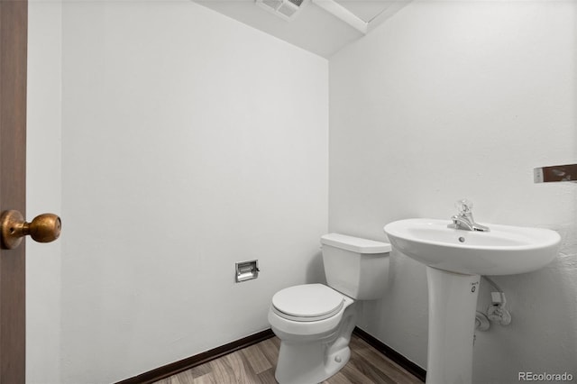 bathroom with toilet, a sink, wood finished floors, visible vents, and baseboards