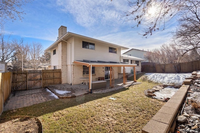 back of property featuring a patio, a fenced backyard, brick siding, a lawn, and a chimney