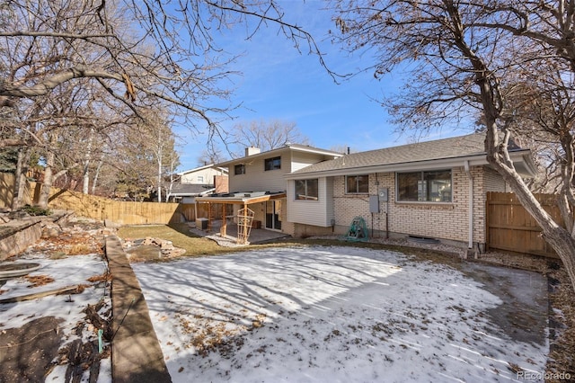 snow covered property featuring a fenced backyard, brick siding, and a chimney