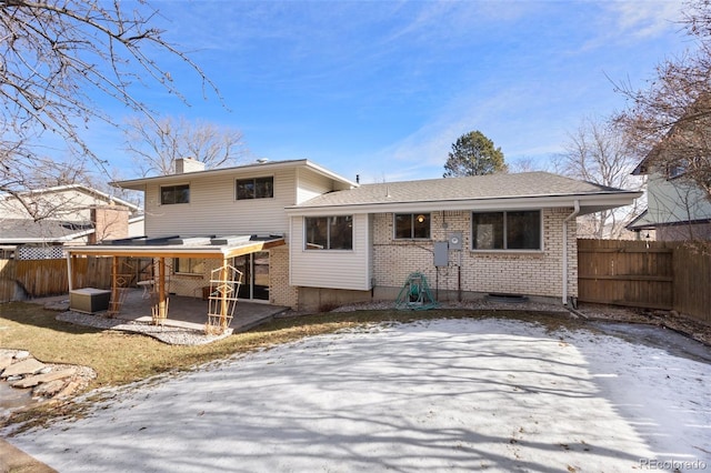 snow covered rear of property with a patio, brick siding, a chimney, and fence