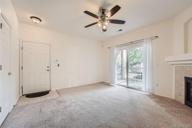 unfurnished living room featuring a tile fireplace, ceiling fan, and light colored carpet