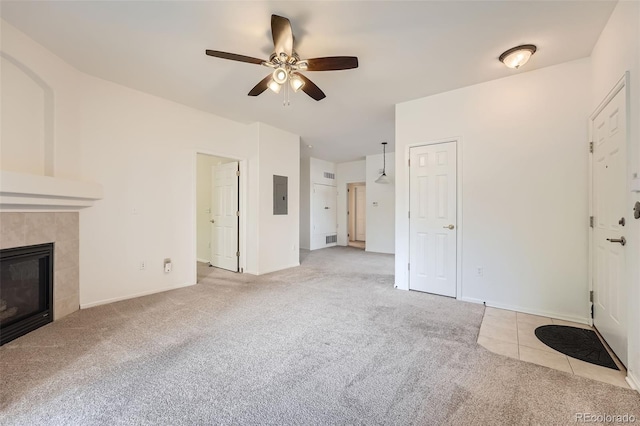 unfurnished living room featuring a tiled fireplace, ceiling fan, light colored carpet, and electric panel