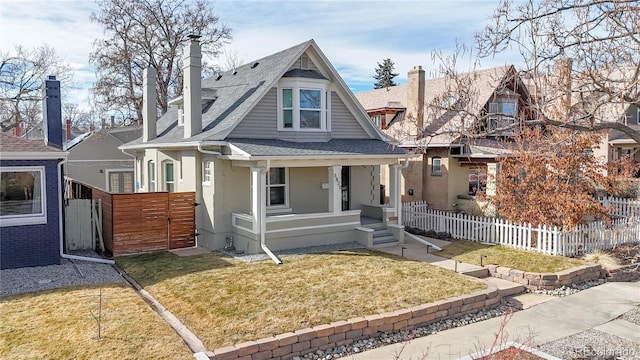 view of front of property with a porch, roof with shingles, a front yard, and fence