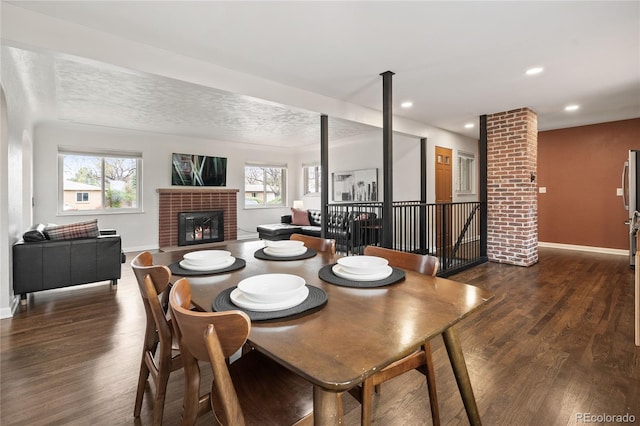 dining area featuring baseboards, a brick fireplace, and dark wood-style floors